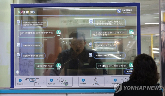 지난해 12월 서울 지하철 4호선 명동역에 투명한 유기발광다이오드(OLED) 디스플레이를 사이에 두고 외국인과 역 직원이 각각 자국어로 대화하는 외국어 동시 대화 시스템이 시범 운영되고 있다. <연합뉴스 제공>